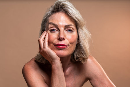Beauty portrait of beautiful mature woman, concepts about cosmetics, skincare and wellness. Beautiful mature woman with blond hair and bare shoulders. Posing with her hand on her faceの写真素材