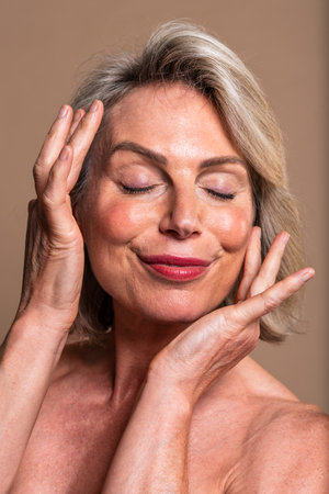Beauty portrait of beautiful mature woman, concepts about cosmetics, skincare and wellness. Mature woman with closed eyes and a peaceful expression gently touching her faceの写真素材
