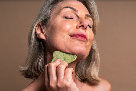 Beauty portrait of beautiful mature woman, concepts about cosmetics, skincare and wellness. Mature woman receiving gua sha facial massageの写真素材