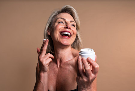 Beauty portrait of beautiful mature woman, concepts about cosmetics, skincare and wellness. Happy mature woman laughing while applying moisturizerの写真素材