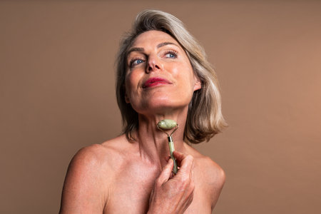 Beauty portrait of beautiful mature woman, concepts about cosmetics, skincare and wellness. Mature woman massaging her neck with a jade rollerの写真素材