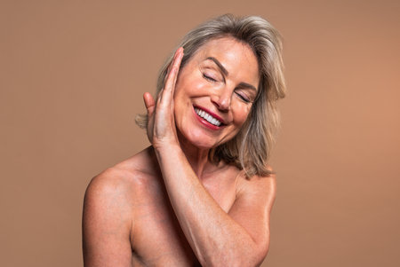 Beauty portrait of beautiful mature woman, concepts about cosmetics, skincare and wellness. Smiling mature woman caressing her face in a studio portraitの写真素材