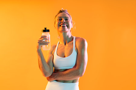 Beautiful mature sportive woman wearing sportswear doing workout - smiling mature sportswoman enjoying hydration after exercising, embodying vitality and promoting a healthy, active lifestyleの写真素材
