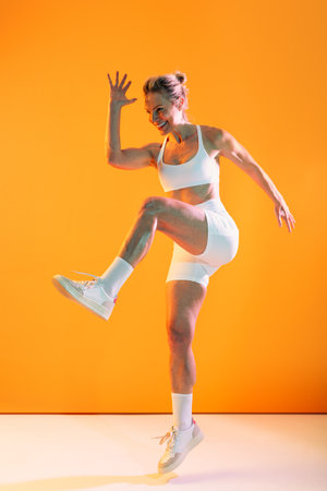 Beautiful mature sportive woman wearing sportswear doing workout - happy athletic mature woman wearing sportswear, jumping and smiling while enjoying her fitness workout against an orange backgroundの写真素材