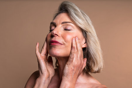 Beauty portrait of beautiful mature woman, concepts about cosmetics, skincare and wellness. Mature woman with closed eyes and a serene expression gently touching her faceの写真素材