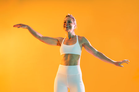 Beautiful mature sportive woman wearing sportswear doing workout - mature woman exercising in sportswear against a vibrant orange backdrop, radiating energy and vitality in a colorful settingの写真素材