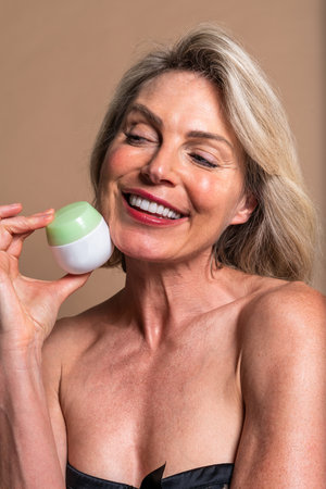Beauty portrait of beautiful mature woman, concepts about cosmetics, skincare and wellness. Happy mature woman applying anti-aging cream. Enjoying her skincare routine for healthyの写真素材
