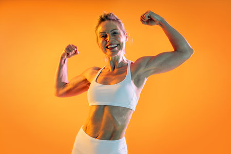 Beautiful mature sportive woman wearing sportswear doing workout - happy senior athlete flexing...