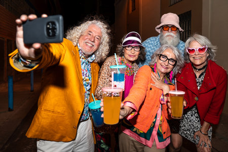 Group of happy senior friends with fancy clothing having party in the night on city streets -...