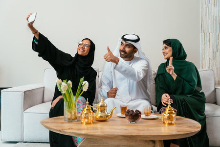 Three emirate friends, two women in abayas and a man in a kandura, enjoying tea and dates while...