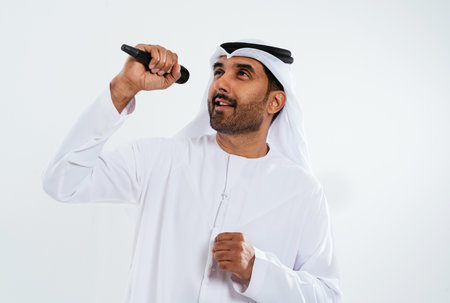 Middle-eastern businessman in traditional white kandura singing into a microphone during a conference in a studioの写真素材