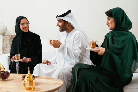 Emirati friends, dressed in traditional abayas and kanduras, relaxing on a modern sofa while...