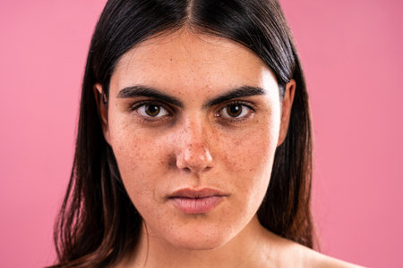 Studio portrait of a young woman with freckles showing her unique style against a vibrant pink...