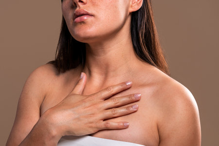 Beautiful young woman with long brown hair and tattoos is touching her chest and showing her healthy...