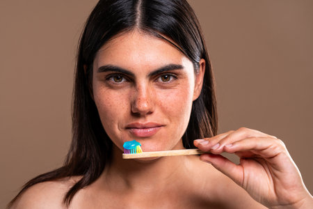 Studio portrait of a beautiful young woman with freckles holding a wooden toothbrush with blue...