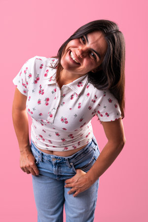 Cheerful young woman with long brown hair, smiling in a floral print top and jeans, leaning forward...