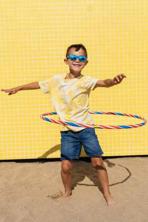 Happy and cool young boy having fun at the beach during summertime - Asian kid wearing sunglasses and swimwear portrait on a yellow background wallの写真素材