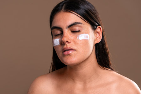 Young woman with closed eyes is receiving a beauty treatment with moisturizing cream applied on her face, promoting skincare and body care conceptsの写真素材
