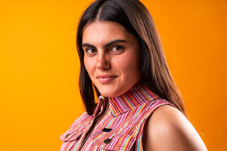 Portrait of a young woman with a distinct fashion sense, set against a vibrant orange background. Her confident expression and colorful attire reflect individuality and modern styleの写真素材