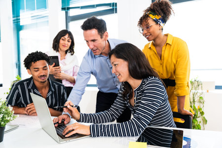 Business team collaborating on a project, using a laptop, in a modern startup office, working...