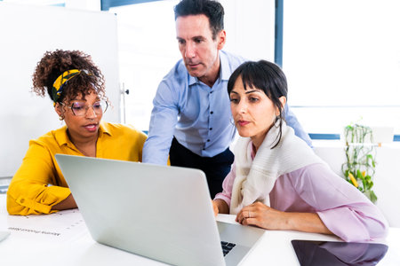 Business team working together on a project, analyzing data on a laptop in a bright modern office,...