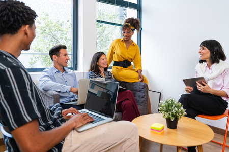 Five business people are having a productive meeting in a modern office, using laptops and tablets,...