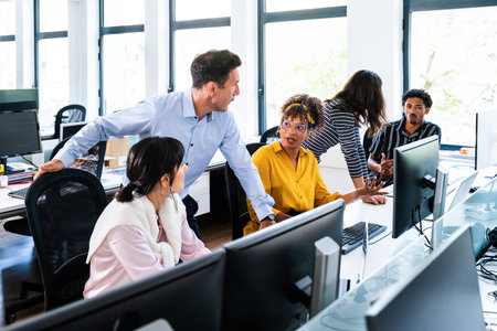 Office workers discussing a project, collaborating and engaging with desktop computers in a bright,...