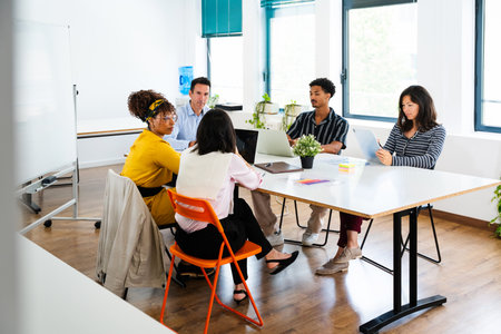Diverse team of professionals working together on project, sharing ideas and using laptop during...