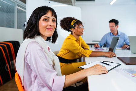 Business team collaborating on project during meeting in modern office, using laptops and taking...