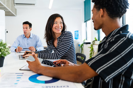 Business team members are discussing a project, using digital tablets and laptops in a modern...