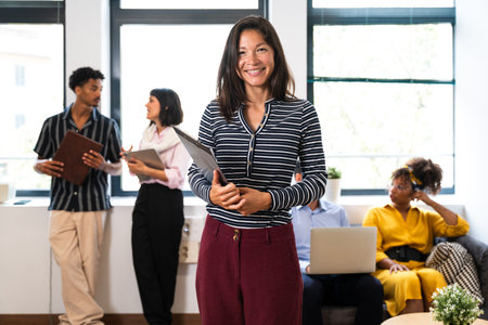 Confident businesswoman smiling and holding a clipboard leading a business meeting with her diverse...