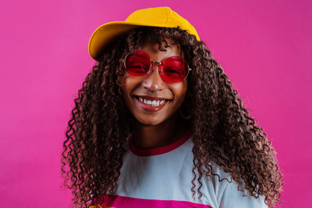 Studio shot of a cheerful young woman with long curly hair wearing a rainbow t-shirt, yellow...