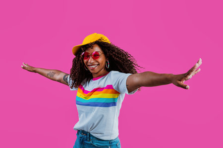 Studio shot of a cheerful young woman with long curly hair wearing a rainbow t-shirt, yellow...