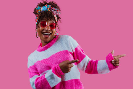 A woman wearing sunglasses and a cozy sweater, laughing joyfully while pointing sideways with index...