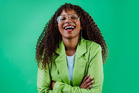Studio portrait of a cheerful young woman with curly hair, wearing a green jacket, smiling on a...