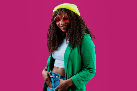 Cheerful young woman with curly hair, wearing a bright green jacket, light blue top, yellow woolen...