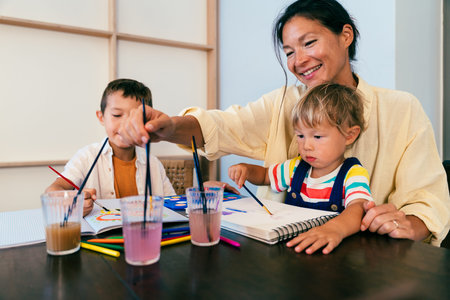 Asian family at home - asian mother and her kids enjoying a creative pastime, painting with...