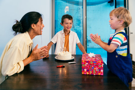 Asian family at home - asian mother and children celebrate a birthday at home, clapping and smiling...