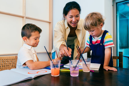 Asian family at home - asian mother guiding two young children painting together at home, fostering...