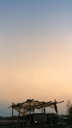 A rustic hut silhouetted against the colorful twilight sky at Cemara Beach, Jember. The fading light from dusk to night creates a peaceful, reflective coastal sceneの写真素材