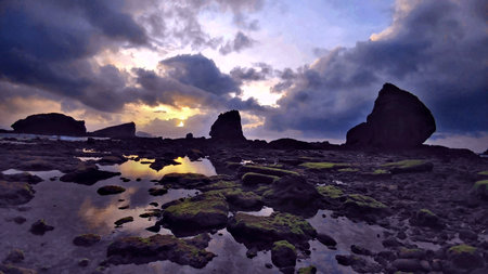 Low-light wide-angle shot of Papuma Beach at dawn, with vibrant skies, calm sea, and textured tidal rocksâcreating a serene, expansive coastal landscape full of natural grandeur.の写真素材