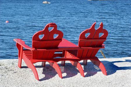 A pair of red wooden Adirondack chairs on the granite rocks overlooking the Atlantic Ocean in Nova Scotia, Canadaの写真素材