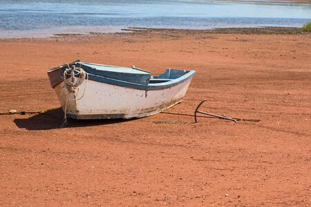 A small boat with its anchor laying on a sandy shore.の写真素材