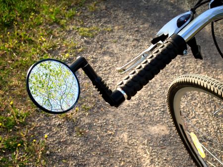 A rear view mirror of a bicycle pointed towards the treetops and sky.                               の写真素材