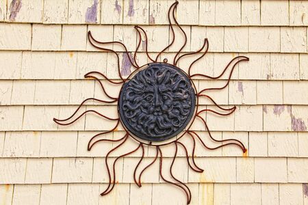 A rusty panel ornament of a stylized sun and face on a wall of peeling shingles.の写真素材