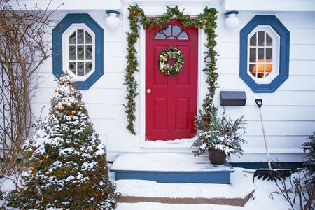 Snow is falling on the front of a tradional house decorated for Christmas with a wreath, garlands and Christmas lights.の写真素材