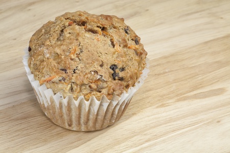 A healthy whole grain carrot raisin muffin with bran on a wooden surface.の写真素材
