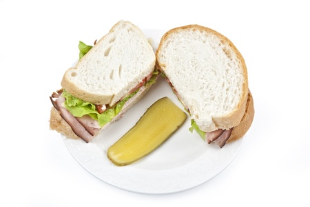 Fresh ham and cheese sandwich and a dill pickle served on a white porcelain plate.の写真素材