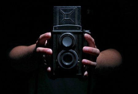 Vintage twin reflex camera held by two hands on black.の写真素材