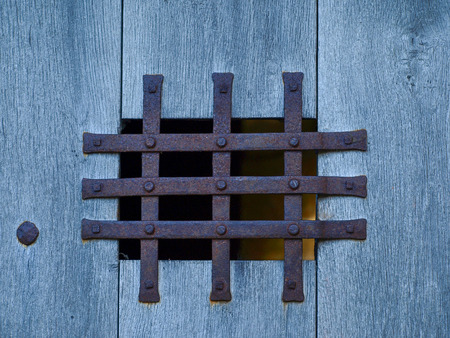 Small window with rusted iron grill on the blue wooden structured wall.の写真素材
